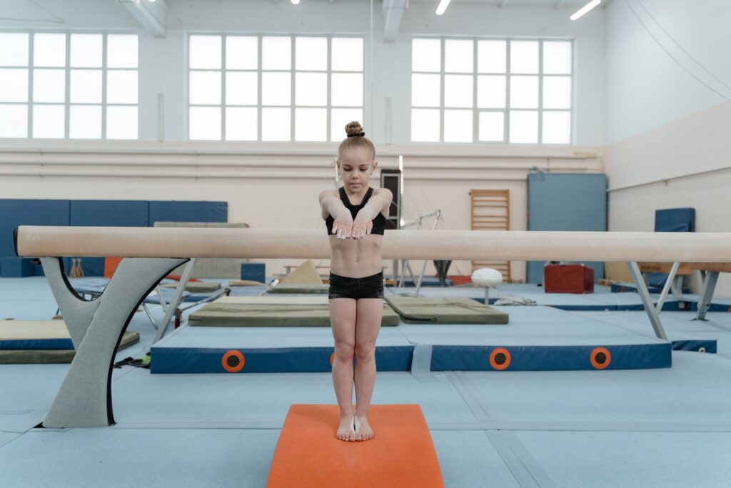 A young girl focuses while performing a balance beam routine in a gym. Gymnastics and training setting.