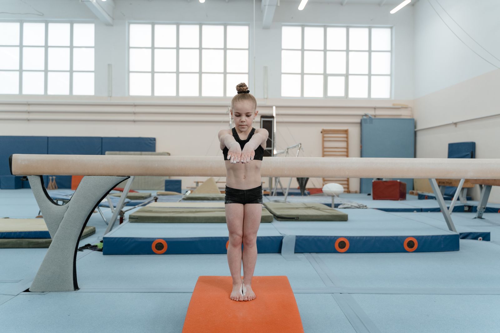 A young girl focuses while performing a balance beam routine in a gym. Gymnastics and training setting.